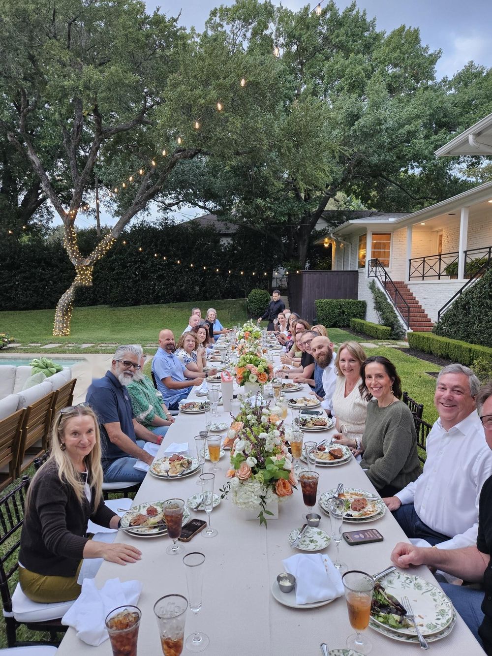 The LAM Technology team seated along a long table outdoors at the 20th anniversary dinner, string lights overhead.